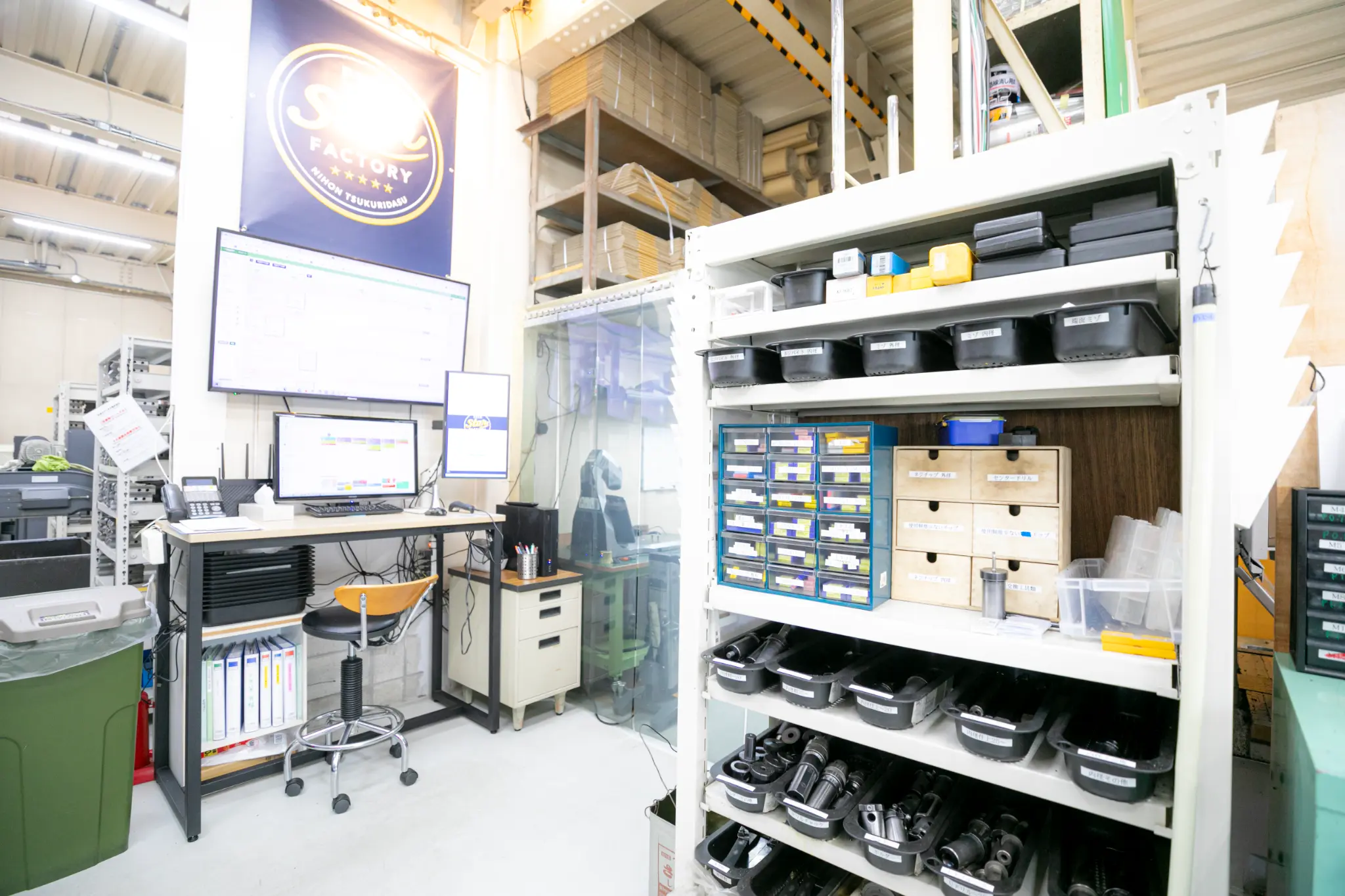 エムネットくらうどの画面と工具棚がある工場内