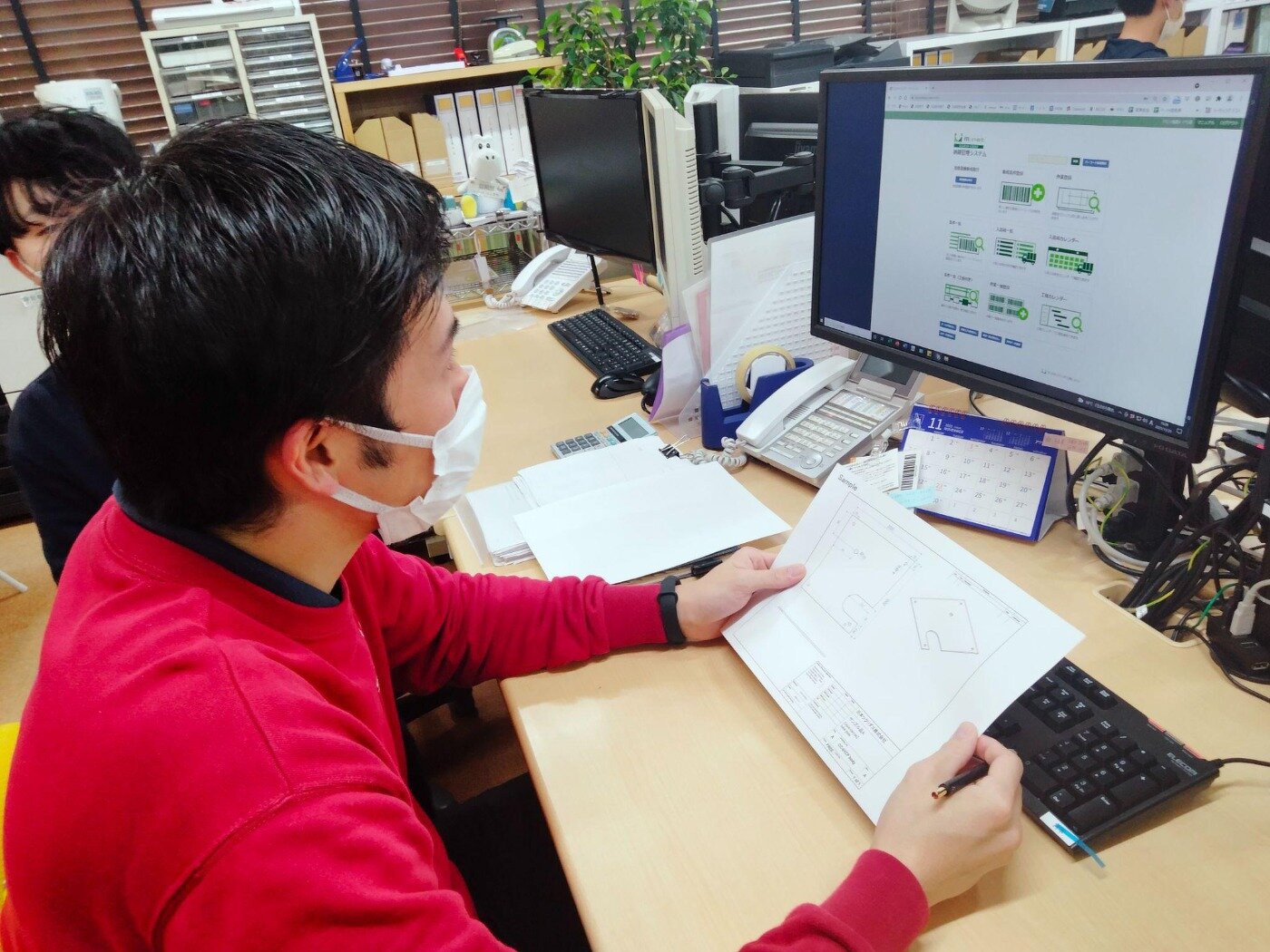 手元の図面を確認しながら、PC画面の生産管理システム『エムネットくらうど』へ案件情報を入力する担当者