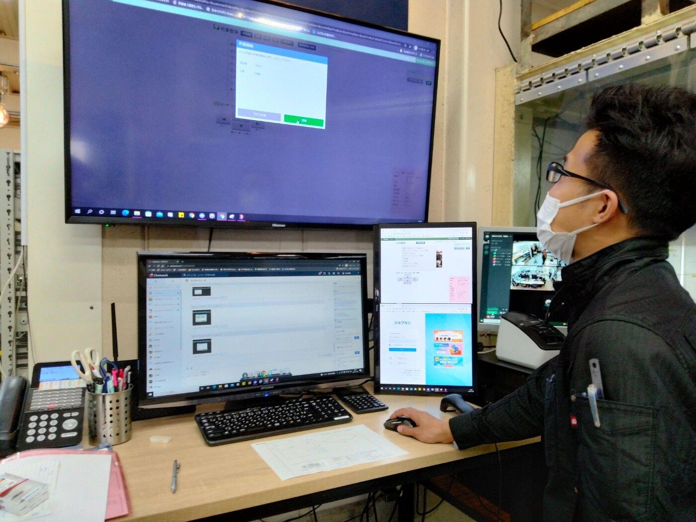 複数のモニターが設置されたデスクで、エムネットくらうどのシステム画面を操作して作業終了の登録を行う担当者
