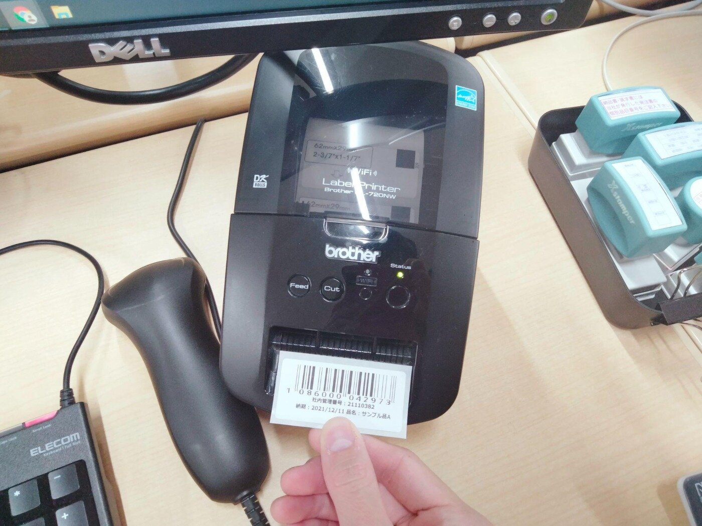 ラベルプリンターから印刷されたバーコード付きの管理ラベルを手に取る様子